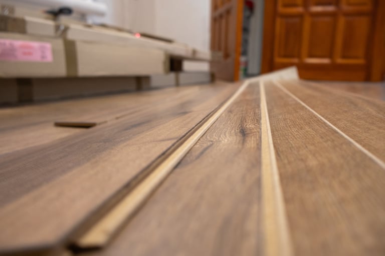Workers are laying down laminate flooring in a well-lit room featuring wooden doors and modern decor elements